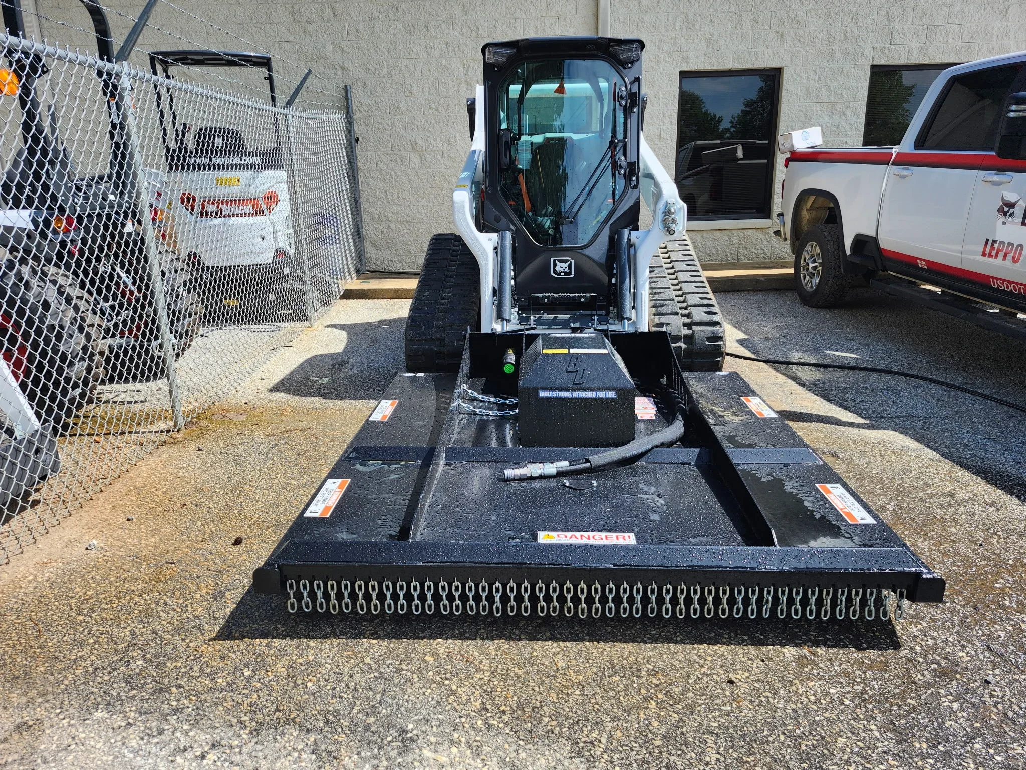 Skid steer loader with black hydraulic sweeper attachment on flatbed trailer